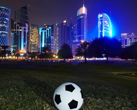Foto af Qatars skyskrapere og en fodbold på en græsplæne.