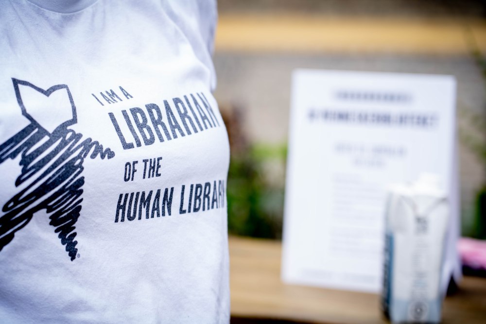 Foto af en t-shirt fra Menneskebiblioteket, båret af en bibliotekar, der står for udlån og påtrykt: "I am a librarian of the Human Library"..