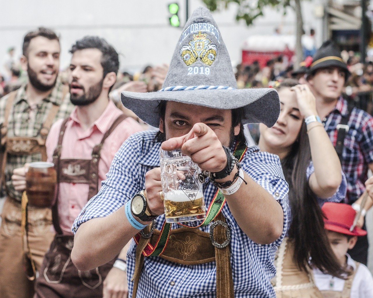 En mand i sydtysk outfit med et ølkrus i den ene hånd peger finger ad beskueren med den anden.