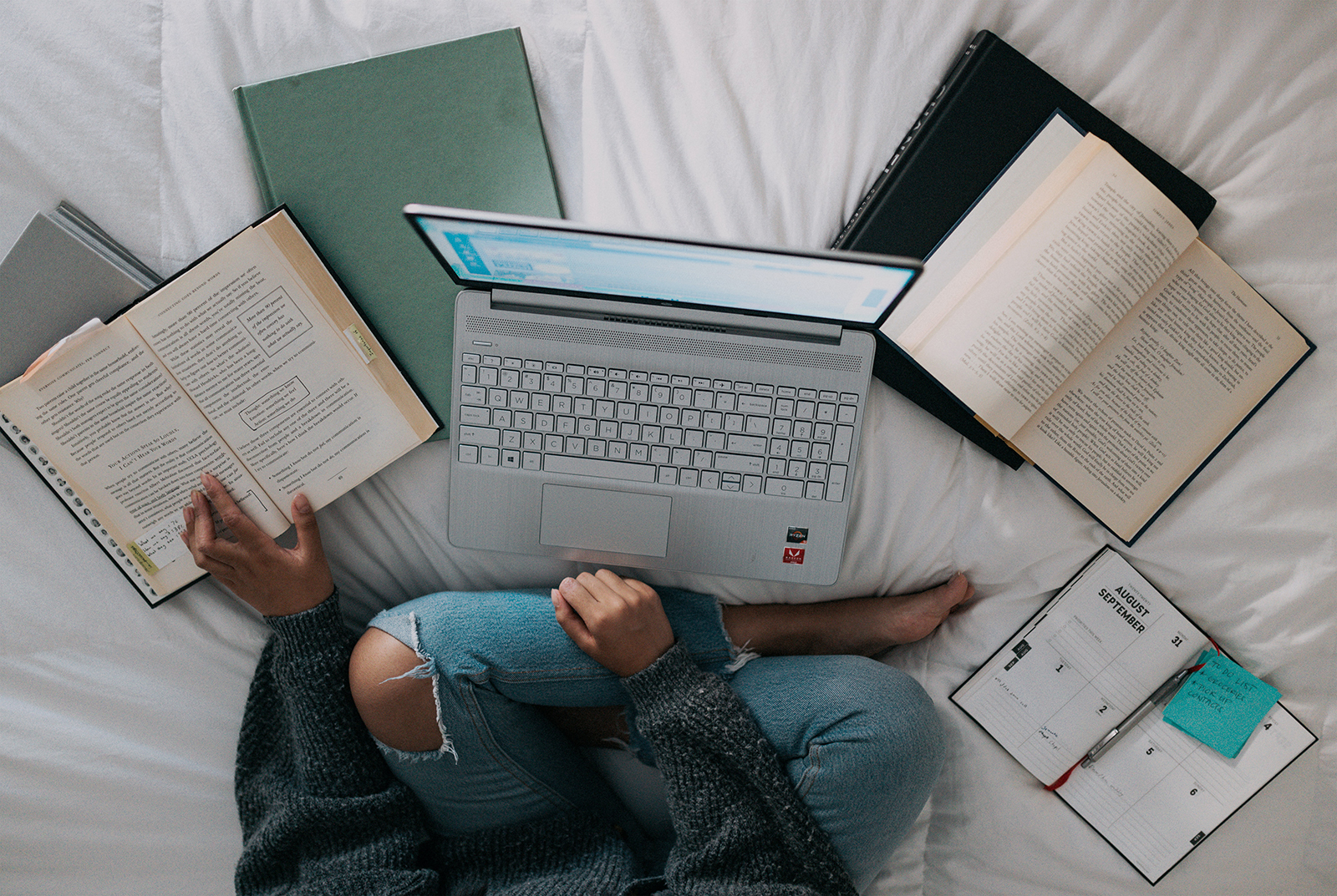 Studerende med laptop og bøger på sengen