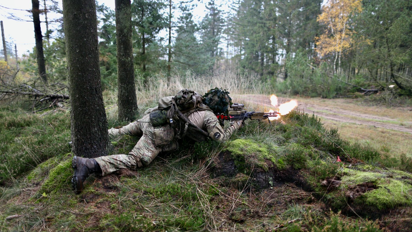 Soldat i forsvaret på øvelse i skov, affyrer maskingevær