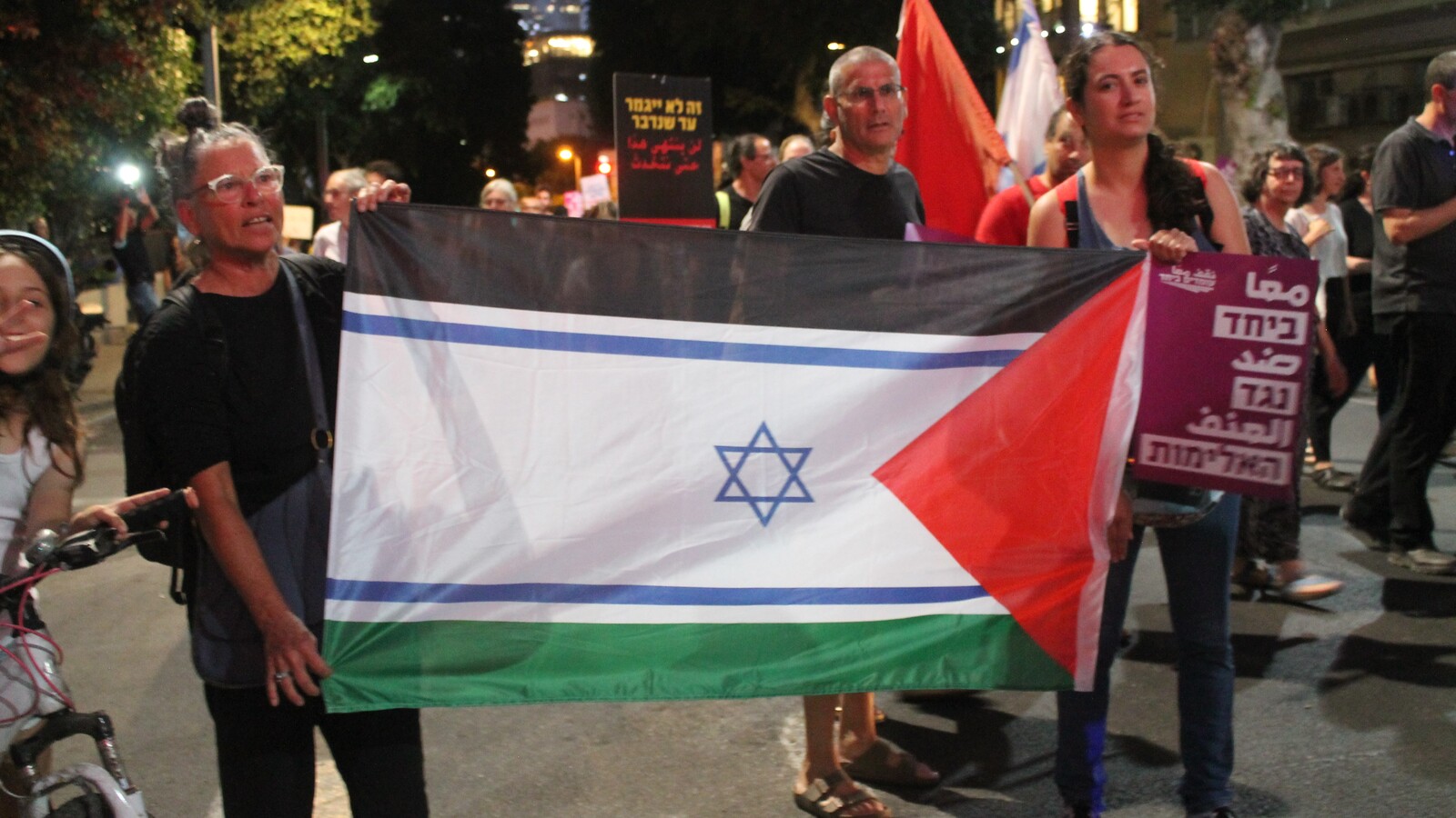 Foto fra en demonstration i israelske Tel Aviv. En mand og en kvinde holder et flag, der kombinerer det israelske og det palæstinensiske flag.