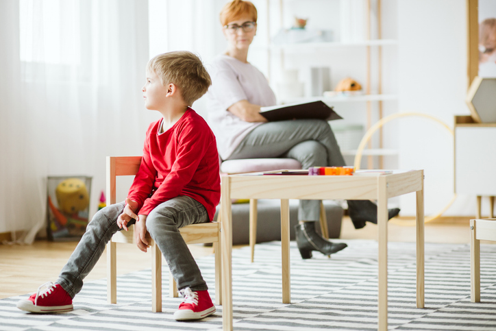 Foto af dagdrømmende dreng i klasseværelse og en voksen, der iagttagelser ham, med en mappe i skødet. Fotoet illustrerer en igangværende udredning af ADHD. 