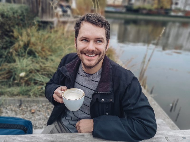 Foto af glad og smilende mand med en kop kaffe i det fri.