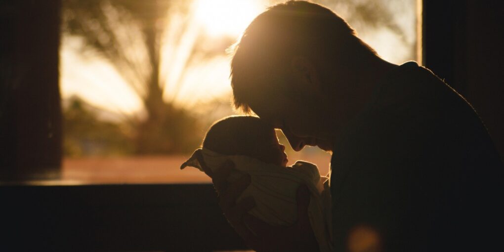 Foto af nyfødt i armene på sin far som illustration af Hannah Arendts begreb, natalitet, og sollys som håb om fred.